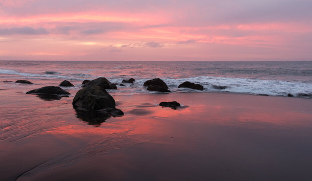 Pink Sunset Reflected on Wet Sand Along a Rocky Beach