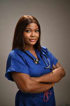 Confident Black female nurse wearing blue scrubs and a stethoscope, arms crossed in a professional portrait. Calm, competent medical professional conveying trust, leadership, and compassionate patient