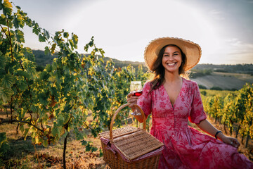 Obraz premium Woman sitting in vineyard with picnic basket and glass of red wine