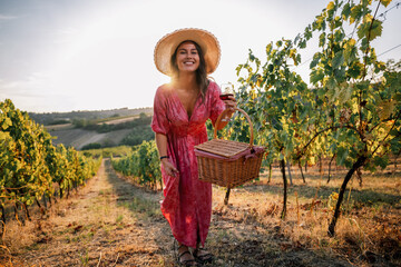 Obraz premium Happy woman walking towards camera holding picnic basket in vineyard