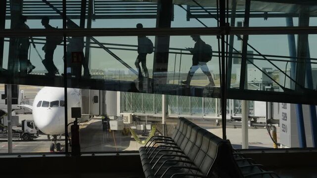 Passengers with luggage crossing glass airport walkway above parked plane in Madrid