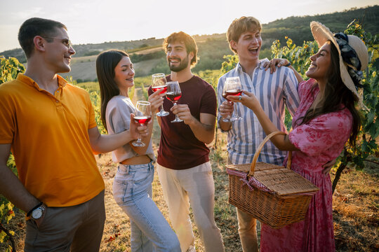 Young people enjoying wine tasting together in sunset vineyard row