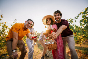 Obraz premium Group of friends reaching out with wine glasses for a toast in vineyard