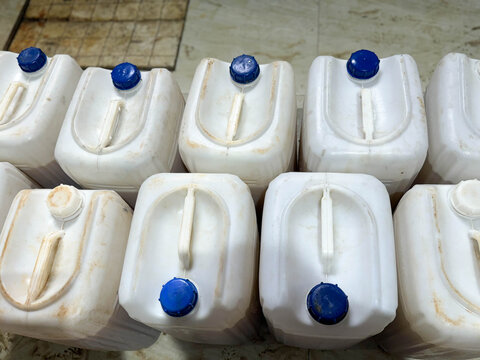 White plastic jerry cans with blue caps stacked in an industrial facility