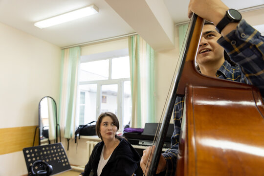 A male double bass player and a female guitarist sharing a light moment during a music college rehearsal.