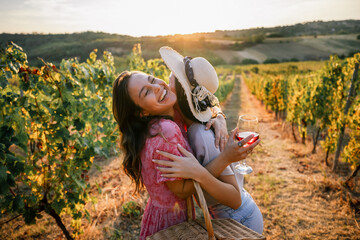 Obraz premium Two joyful female friends hugging tightly with wine in vineyard sunset