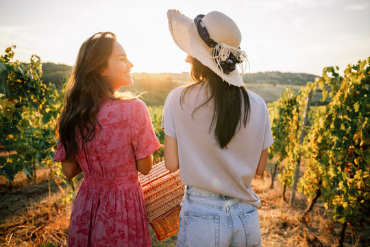 Back view of two female friends walking with picnic basket in vineyard