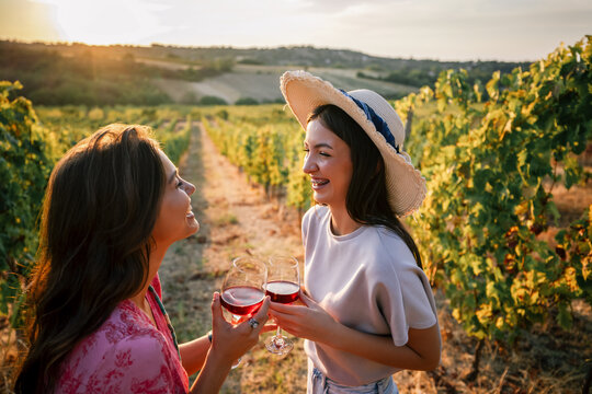 Two women toasting with wine glasses and smiling in a sunset vineyard