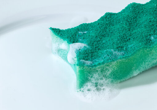 Close-Up of Soapy Green Sponge Dripping Foam on White Plate