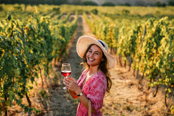 Obraz premium Happy woman smiling at camera holding glass of red wine in vineyard