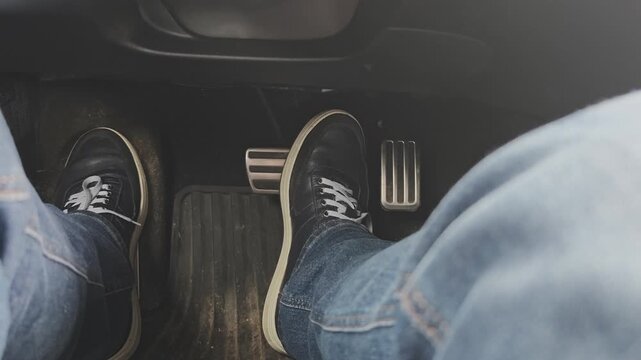 Close up of a man's feet in sneakers and jeans pushing the gas and brake pedals. A driver operating an automatic transmission car