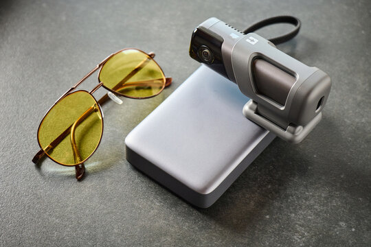 Sunglasses and video camera placed on a gray surface with a portable charger in background