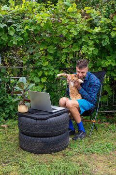 Man Working Outdoors with Cat and Laptop on Upcycled Tires