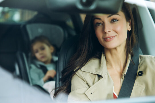 Smiling beautiful mother driving car with daughter in child seat