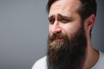 Close-up portrait of a bearded man with a long beard and pensive expression, soft lighting and neutral background conveying thoughtfulness, introspection and quiet emotion. © Loginova