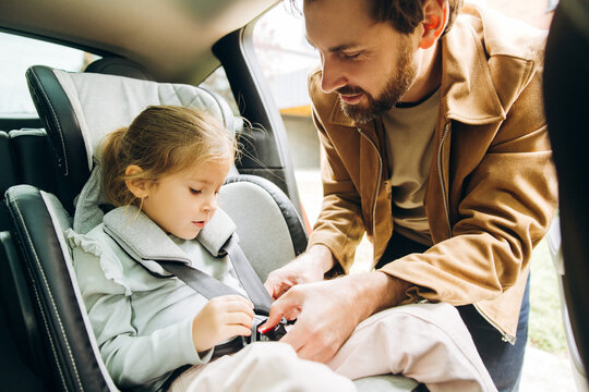 Handsome father buckling child into car seat for safe travel