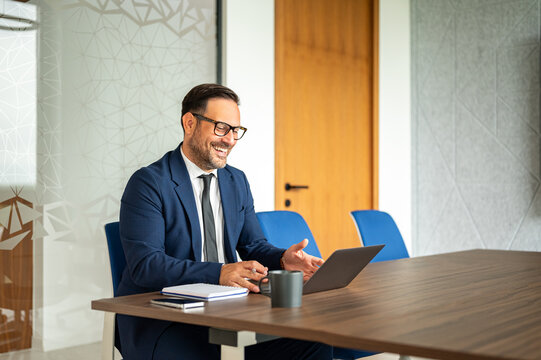 Professional man smiling and gesturing while participating in an online discussion on his laptop, demonstrating engagement and positive communication in an corporate meeting setting