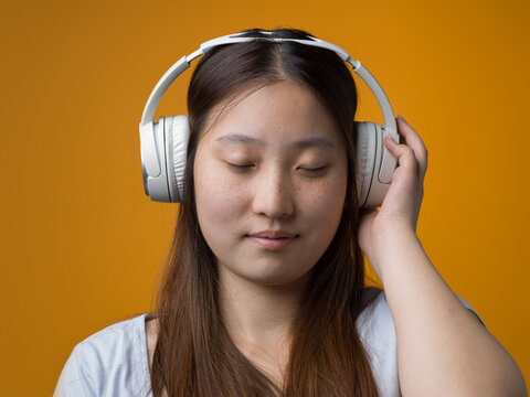 Young Chinese Woman Enjoying Music with Closed Eyes and Wireless Headphones