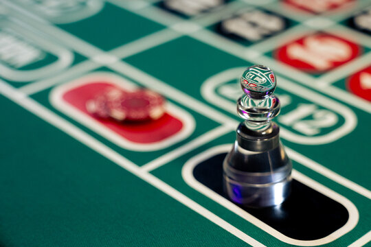 Glass dolly marker and red chips rest on green casino roulette table surface. Photo shows the danger of gambling addiction and financial risk.