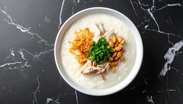 A delicious bowl of traditional Asian chicken rice congee served with peanuts and crispy shallots on a dark marble tabletop