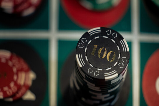 Close up top view of black one hundred casino chips stack on green roulette table. Photo highlights the danger of gambling addiction and money loss risk.