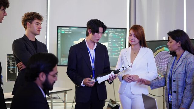 Asian engineer in suit hands a bionic robotic arm to a woman in white blazer as colleagues look on around the table, at a key moment of the test, a humanoid robot engineering concept