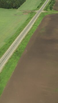 Drone footage of a straight country road cutting through green fields, dark plowed farmland and forest edge in the Ural Mountains region, Russia, summer countryside