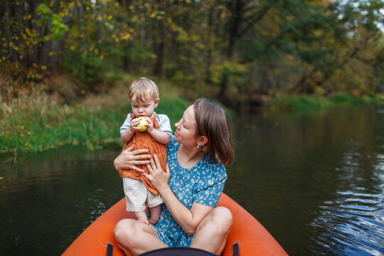A mother holds an infant under one year old who is eating an apple on a kayak river trip