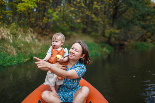 Mother holding an infant child under one year old pointing ahead while riding an orange kayak