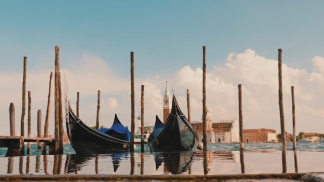 Two gondolas bob gently in Venice canal with distant church tower and fluffy clouds.