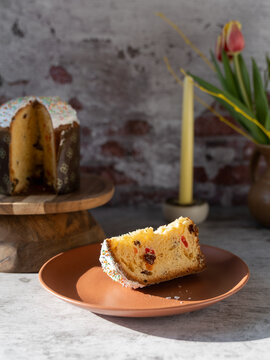 Slice of traditional Paska Pasca Easter bread served on a plate with tulips candles and the remaining Easter bread in the background against a rustic brick wall
