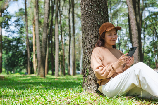 Portrait image of a woman holding and using mobile phone while sitting in the park