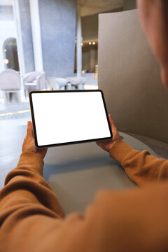Vertical mockup image of a woman holding digital tablet with blank white desktop screen in cafe