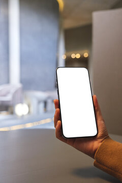 Vertical mockup image of a woman holding mobile phone with blank desktop screen in cafe