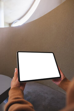 Vertical mockup image of a woman holding digital tablet with blank white desktop screen in cafe
