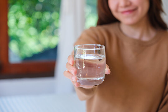 Closeup image of a woman holding and serving a glass of drinking water