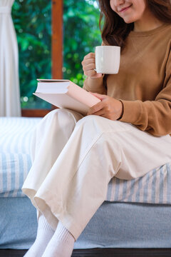 Vertical closeup image of a woman reading a book on the bed at home
