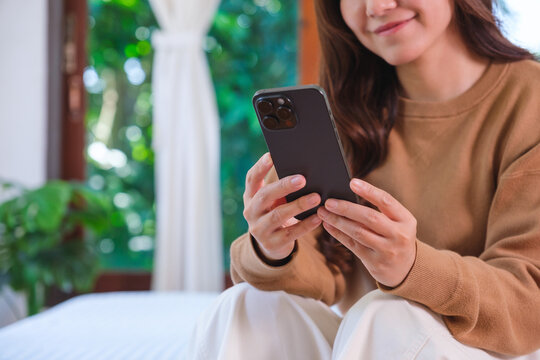 Closeup image of a woman holding and using smart phone on the bed at home