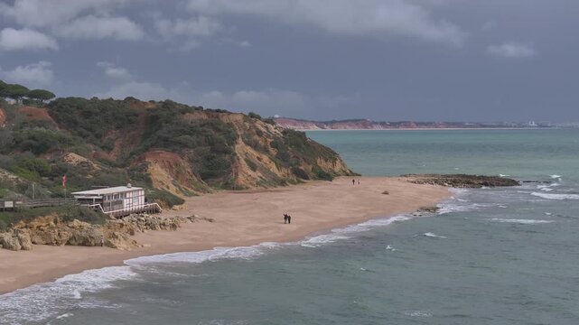 Aerial rise over red cliffs and beach in Albufeira under cloudy sky
