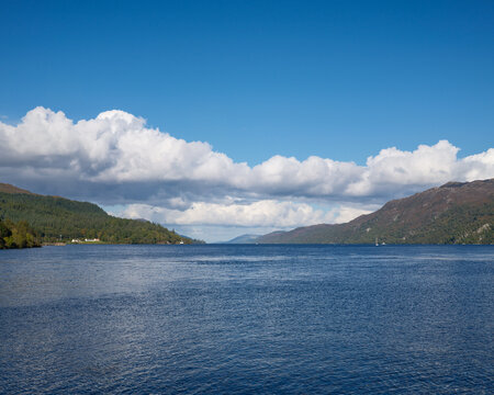 View looking north across the calm waters of Loch Ness from Fort Augustus in the Scottish Highlands on a bright sunny afternoon with clouds above