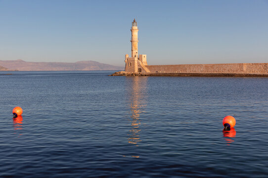 Historic Venetian lighthouse and stone harbor wall illuminated by warm sunrise light in Chania, Crete, Greece.