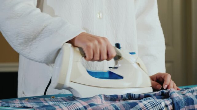 A close-up shot of a person ironing a blue and white plaid shirt on an ironing board, showcasing household chore motion.