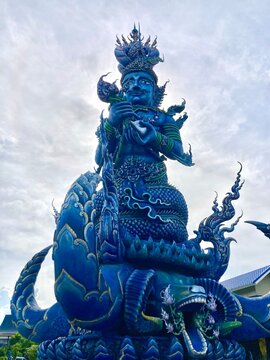 Vertical low angle view of the magnificent blue Deva statue and naga sculpture at Wat Rong Suea Ten in Chiang Rai.