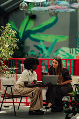 Obraz premium Diverse businesswomen collaborating on laptop, discussing project details in a modern office space