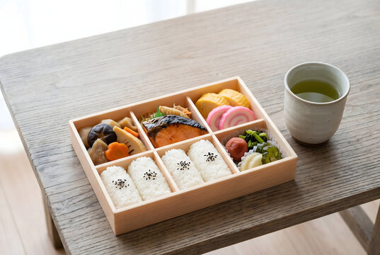 Japanese bento box with rice, grilled salmon and simmered vegetables beside a cup of green tea
