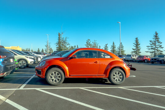 Calgary, Alberta, Canada. September 27, 2026. Side angle of an orange Volkswagen Beetle parked in an outdoor public parking lot.