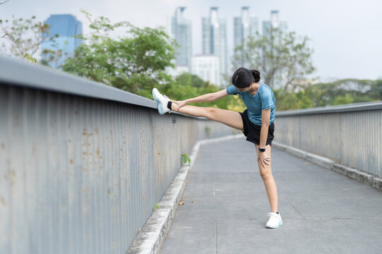 Woman stretching leg on metal railing during outdoor exercise in urban park, flexibility training, warm up, sportswear, smartwatch, fitness routine, wellness, balance, mobility and healthy habit.