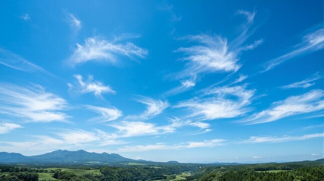 Vast sky stretches wide and bright above rolling hills. Cirrus clouds drift gently, wispy, elegant, serene. Mountains fade softly into distant blue haze. Lush green fields stretch beneath, vibrant