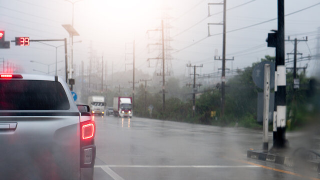 Pickup car stopped in a queue of traffic on a wet asphalt street. During a rainy daytime downpour with overcast skies. Side road with trees and electric pole.