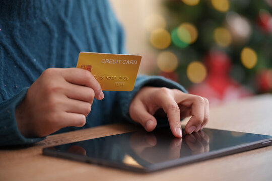 Woman holding a credit card while browsing a tablet during Christmas. Online shopping and digital payment highlight holiday purchases, retail sales and seasonal spending.